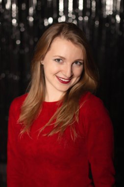 Kırmızı elbiseli çekici kadın bir partide gülümsüyor, gümüş renkli bir arka planda.