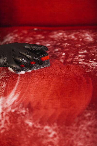 professional cleaning, hand in a glove rubs chemistry with a sponge into the red sofa