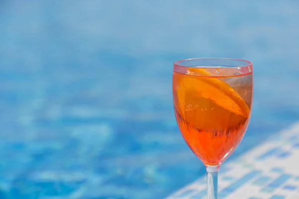 A citrus cocktail stands on the side of a blue pool, copyspace