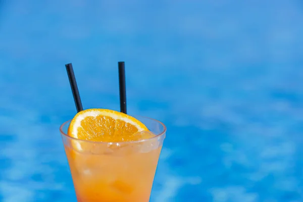 Orange cocktail with two straws on a blue pool background