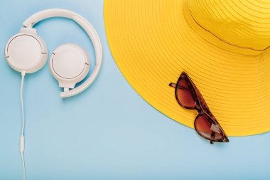 Mavi arka planda güneş gözlüğü, kulaklık ve sarı plaj şapkası, mesaj için yer