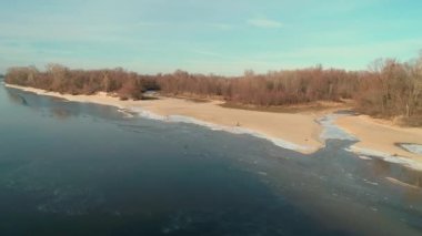 Aerial drone footage of flight over a sandy shore with a small river in winter