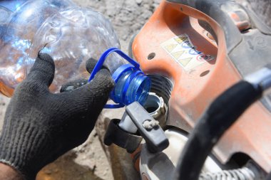 Bir işçi plastik şişeden yakın plan testereye benzin döker..