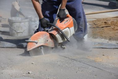Bir işçi, asfaltı dairesel testere ile keser. Yol yüzeyindeki bir borunun değiştirilmesi planlanmıştır..