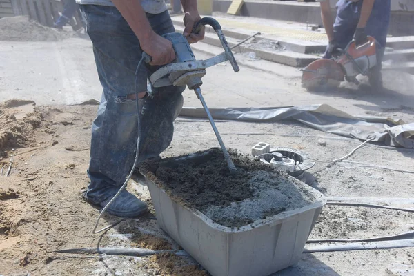 A worker interferes with cement on a construction site, preparing to lay road tiles.