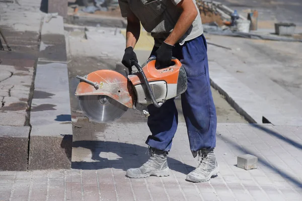 A worker holds a saw, cutting concrete blocks, repairing the road.