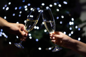 Oslava Vánoc doma, pár cinkajících skleniček se šampaňským a držení jisker na pozadí vánočního stromečku, detailní záběr.