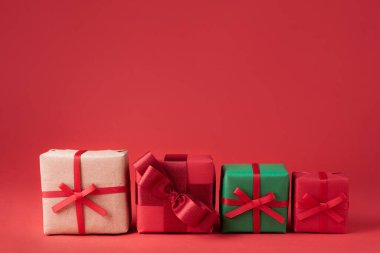 Kırmızı arka planda renkli ambalajlı dört Noel hediyesi, yakın plan..