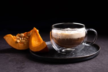 Krem şantili ve balkabağı dilimli, koyu arkaplanda bir bardak balkabağı lattesi..