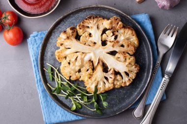 Çatal bıçaklı karnabahar bifteği, gri arka planda sağlıklı vejetaryen yemeği..