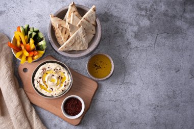 Humuslu kase, doğranmış sebze ve gri arka planda pide, sağlıklı vejetaryen yemeği..