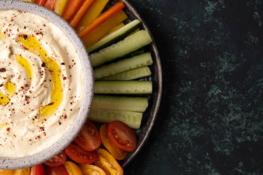 Sağlıklı vejetaryen atıştırmalıkları, humus ve yeşil arka planda dilimlenmiş sebzelerle kase kapağı..