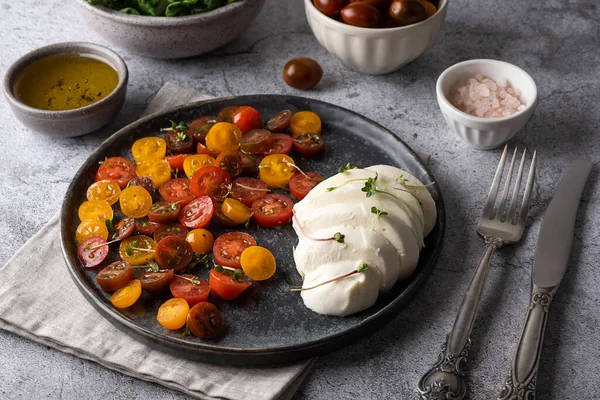 Caprese salatalı gri tabak, dilimlenmiş zeytinyağlı domatesli mozarella peyniri.