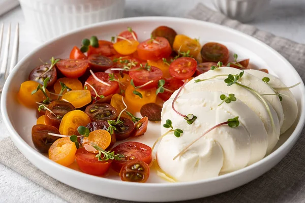 Yakın plan mozzarella top peyniri dilimlenmiş kiraz domatesli, zeytinyağlı, caprese salatalı beyaz tabak.