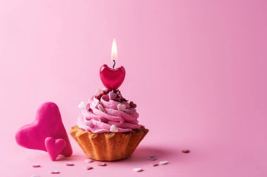 Two hearts and a cupcake with cream and a burning candle on a pink background, Valentine's Day concept.