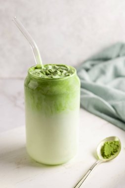 Bir bardak dalgona matcha latte ve beyaz arka planda bir kaşık yeşil çay tozu..