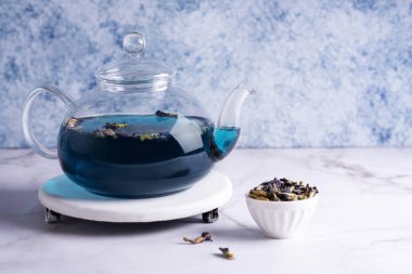 Mavi çaydanlıklı cam çaydanlık mavi arka planda kuru kelebek bezelyesi çiçeği, sağlıklı bitkisel içecek..