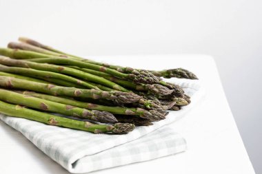 Beyaz arka planda havlunun üzerinde yeşil kuşkonmaz, çiğ sebze, sağlıklı vegan yemeği..