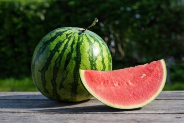 Tahta arka planda dilimlenmiş karpuz, güneş altında yaz meyvesi..