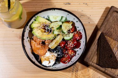 Salmon Poke Bowl with avocado, cucumber , rice and sesame seeds served in bowl, sushi bowl, healthy food, top view.