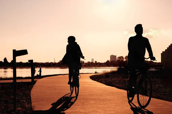 Active leisure in the city at sunset, silhouettes of a woman and a man on a bicycle riding along the river.