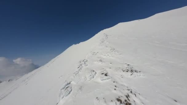 Lezení v blízkosti měkké hladké sněhové pokrývky povrch na vysoké horské hřeben vrchol pod modrým nebem letecký pohled — Stock video