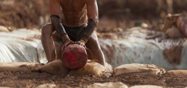 Çamur yarışçıları. Ağaç gövdesindeki katılımcılar, su dolu çukurun üstünde dengeyi yakalıyor.