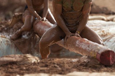 Çamur yarışçıları. Ağaç gövdesindeki katılımcılar, su dolu çukurun üstünde dengeyi yakalıyor.