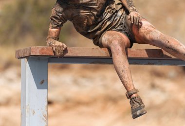 Çamur yarışı. Erkek yarışçı engelleri aşıyor, engelli parkurda duvara tırmanıyor.