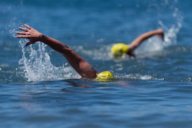 Triatlon yüzücüleri, triatlonda yarışan iki yüzücüyü suda çalkalayıp dururlar.