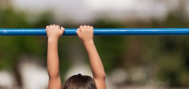 Child playing sports on the playground outdoors, child on the crossbar