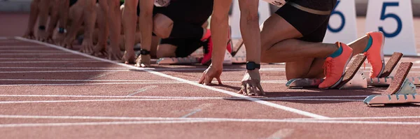 Group of male track athletes on starting blocks. Hands on the starting line. Athletes at the sprint start line in track and field