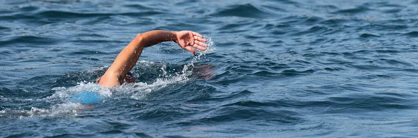 Woman swimmer swimming crawl in blue sea, triathlon competition