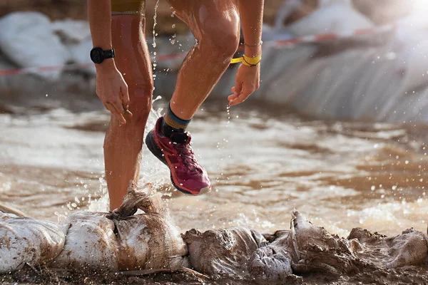 Participant in an obstacle course race runs out of a water obstacle, concept of hardness and effort