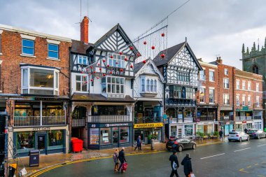 CHESTER, CheSHIRE, İngiltere - 06 Aralık 2021: Tarihi Chester kasabasındaki The Rows dükkanlarının sokak manzarası geleneksel siyah-beyaz kereste çerçeveli Tudor tarzı binalar Noel için dekore edildi