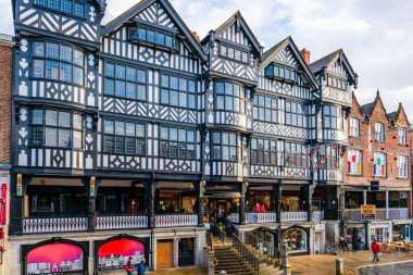 CHESTER, CheSHIRE, İngiltere - 06 Aralık 2021: Tarihi Chester kasabasındaki The Rows dükkanlarının sokak manzarası geleneksel siyah-beyaz kereste çerçeveli Tudor tarzı binalar Noel için dekore edildi