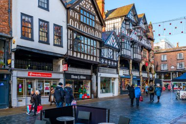 CHESTER, CheSHIRE, İngiltere - 06 Aralık 2021: Tarihi Chester kasabasındaki The Rows dükkanlarının sokak manzarası geleneksel siyah-beyaz kereste çerçeveli Tudor tarzı binalar Noel için dekore edildi