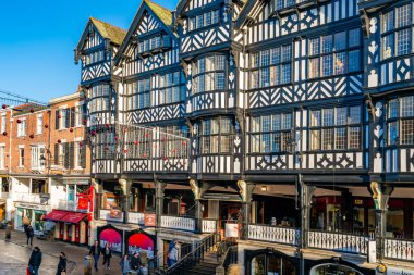 CHESTER, CheSHIRE, İngiltere - 06 Aralık 2021: Tarihi Chester kasabasındaki The Rows dükkanlarının sokak manzarası geleneksel siyah-beyaz kereste çerçeveli Tudor tarzı binalar Noel için dekore edildi