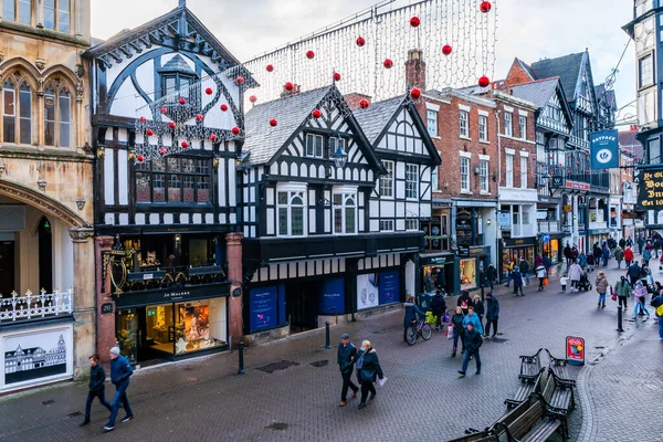 CHESTER, CheSHIRE, İngiltere - 06 Aralık 2021: Tarihi Chester kasabasındaki The Rows dükkanlarının sokak manzarası geleneksel siyah-beyaz kereste çerçeveli Tudor tarzı binalar Noel için dekore edildi