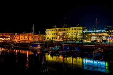TRONDHEIM, NORway - Nidelva nehrine demirlemiş yelkenli tekneleri ve Trondheim şehrine hizmet eden ana tren istasyonu olan Merkezi Tren İstasyonu 'nun gece görüşü