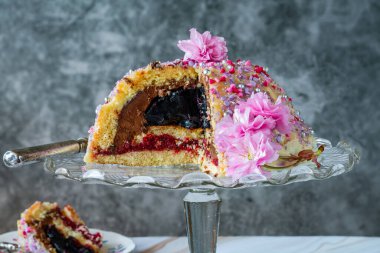 Meyveli jöle, koyu çikolatalı krema ve ahududu püresi ile dolu, beyaz çikolata ganache ile kaplanmış ve renkli süslemelerle süslenmiş.