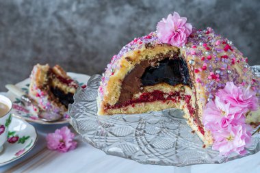 Meyveli jöle, koyu çikolatalı krema ve ahududu püresi ile dolu, beyaz çikolata ganache ile kaplanmış ve renkli süslemelerle süslenmiş.