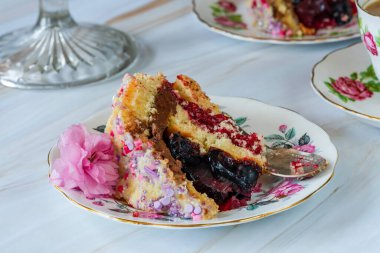 Meyveli jöle, koyu çikolatalı krema ve ahududu püresi ile dolu, beyaz çikolata ganache ile kaplanmış ve renkli süslemelerle süslenmiş.