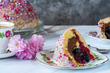 Meyveli jöle, koyu çikolatalı krema ve ahududu püresi ile dolu, beyaz çikolata ganache ile kaplanmış ve renkli süslemelerle süslenmiş.