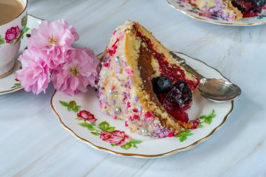 Meyveli jöle, koyu çikolatalı krema ve ahududu püresi ile dolu, beyaz çikolata ganache ile kaplanmış ve renkli süslemelerle süslenmiş.