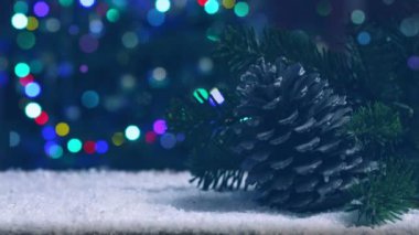 Beyaz kar üzerindeki fidan konisi bulanık Noel ağacı ışıklarının arkasında izole edilmiş..