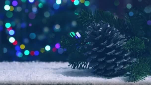 Tannenzapfen auf weißem Schnee isoliert auf unscharfen Weihnachtsbaumlichtern Hintergrund. — Stockvideo