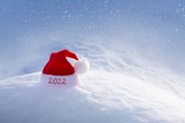 Yeni yıl 2022 arka planı, beyaz kar üzerinde kırmızı Noel Baba şapkası..