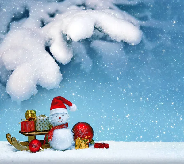 Weihnachten Schneemann mit Geschenken auf dem Schlitten und Schneefall. — Stockfoto