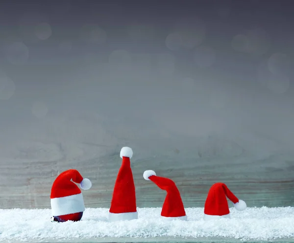 Beyaz kar üzerinde dört kırmızı Noel Baba şapkası . — Stok fotoğraf